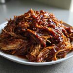 A generous mound of juicy, shredded Slow cooker pulled pork coated in rich barbecue sauce, served on a white plate.