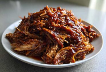 A generous mound of juicy, shredded Slow cooker pulled pork coated in rich barbecue sauce, served on a white plate.