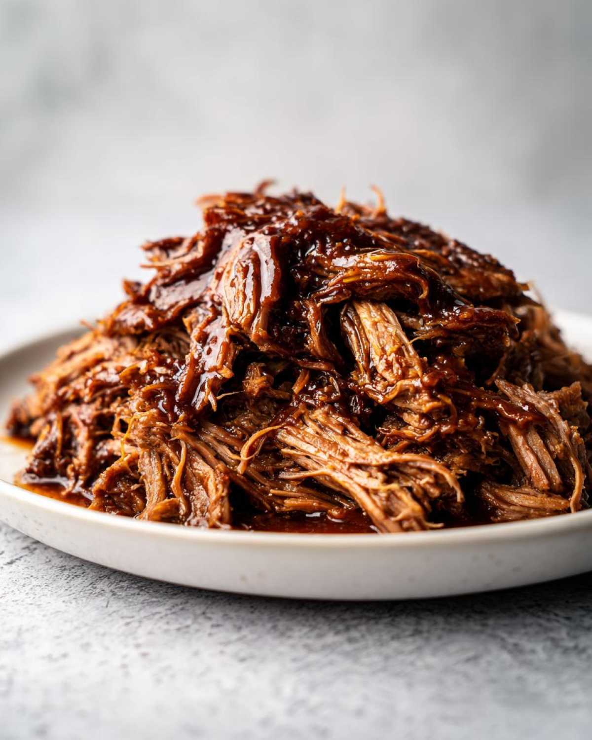 Close-up of tender, shredded Slow cooker pulled pork drenched in rich barbecue sauce on a white plate.