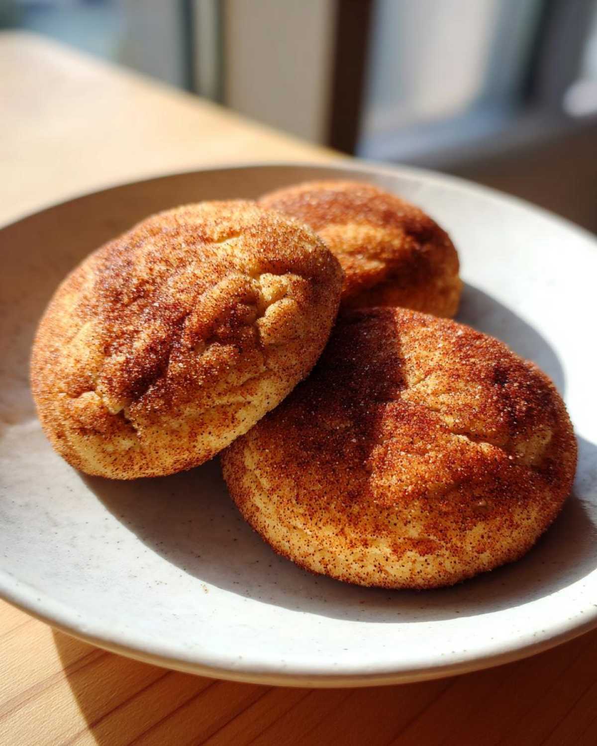 Three soft, thick snickerdoodle cookies heavily coated in cinnamon sugar resting on a light-colored plate.