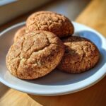 A stack of four soft, chewy snickerdoodle cookies coated in cinnamon sugar, resting on a white plate.