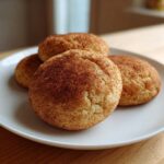 Four perfectly baked, soft snickerdoodle cookies generously coated in cinnamon sugar, resting on a white plate.