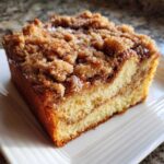 Close-up of a moist slice of sour cream coffee cake featuring a thick, cinnamon streusel topping and glaze.