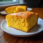 Close-up of a golden slice of moist sourdough cornbread served on a white plate.
