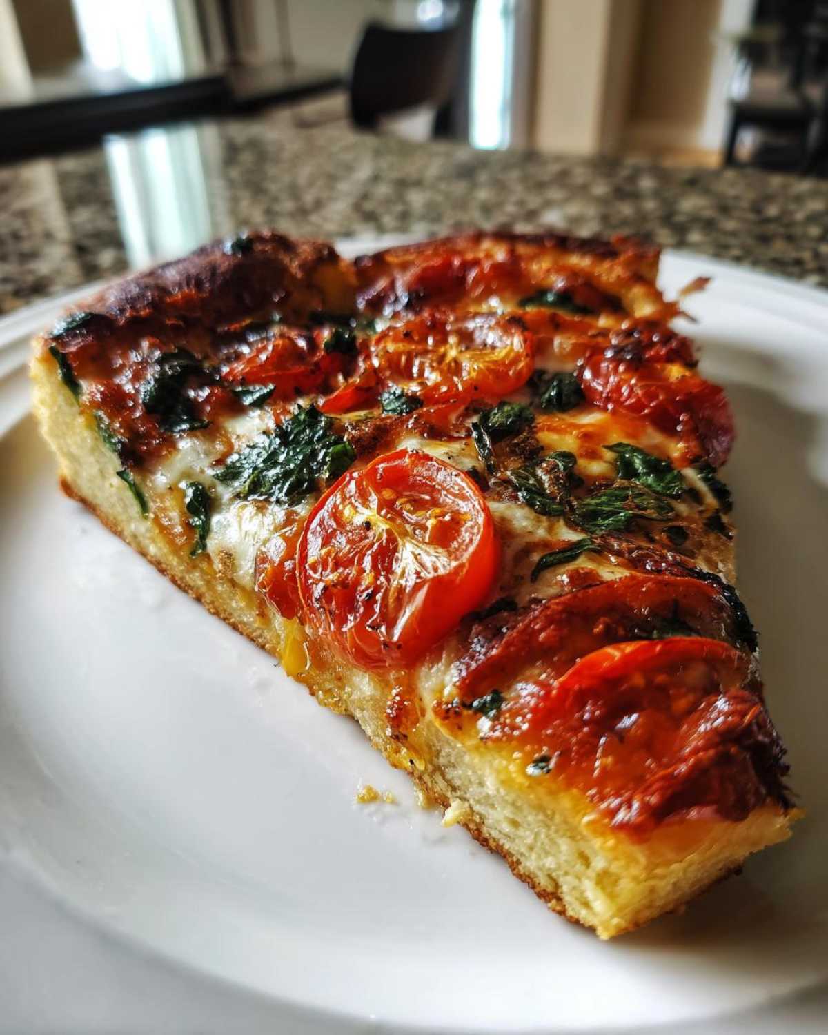 Close-up of a thick slice of pizza with melted cheese, roasted cherry tomatoes, and basil, made from sourdough discard pizza dough.