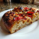 Close-up of a thick, airy slice of sourdough discard pizza dough topped with roasted tomatoes.