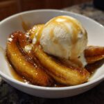 A close-up of warm, caramelized bananas foster topped with a scoop of vanilla ice cream and drizzled with sauce.