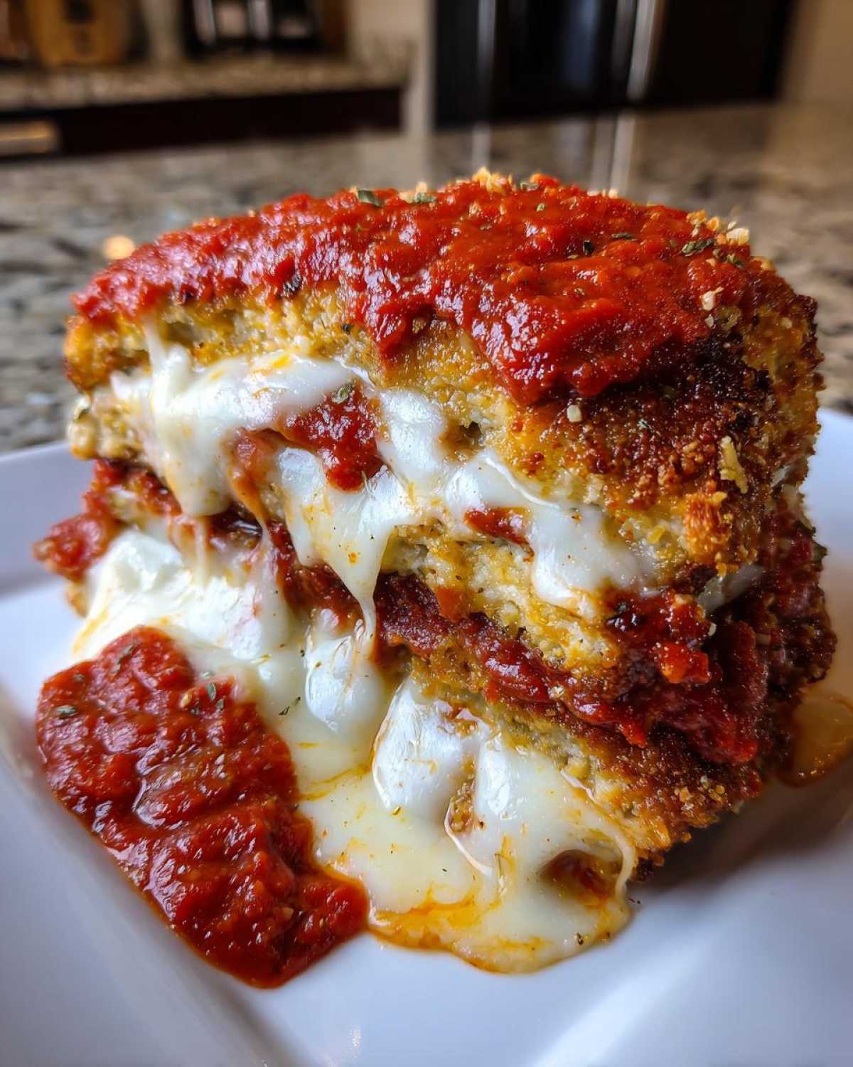 Close-up of stacked, breaded chicken cutlets layered with melted mozzarella and marinara sauce for Easy chicken Parmesan.