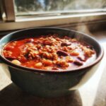 Close-up of a steaming bowl of rich, red high protein chili loaded with ground meat and kidney beans.