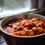 Close-up of a steaming bowl of rich, hearty high protein chili featuring ground meat and beans.