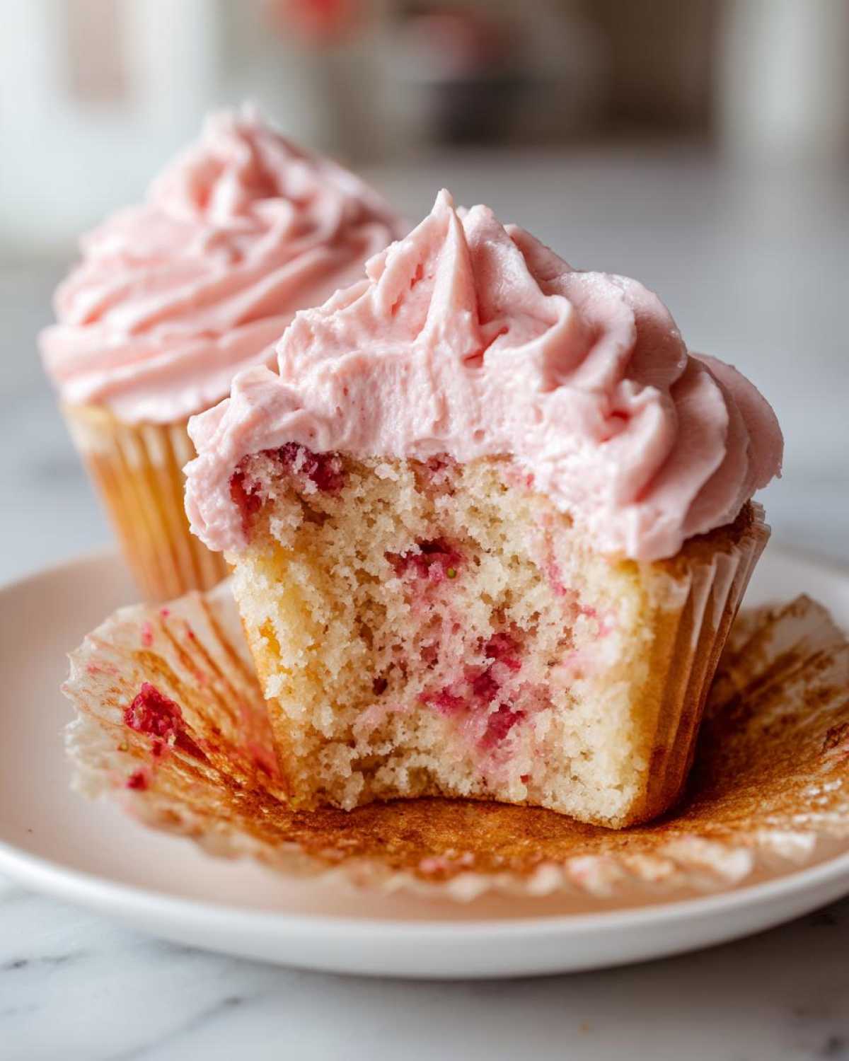 Close-up of a strawberry cupcakes cut in half showing moist cake with berry pieces and pink frosting.