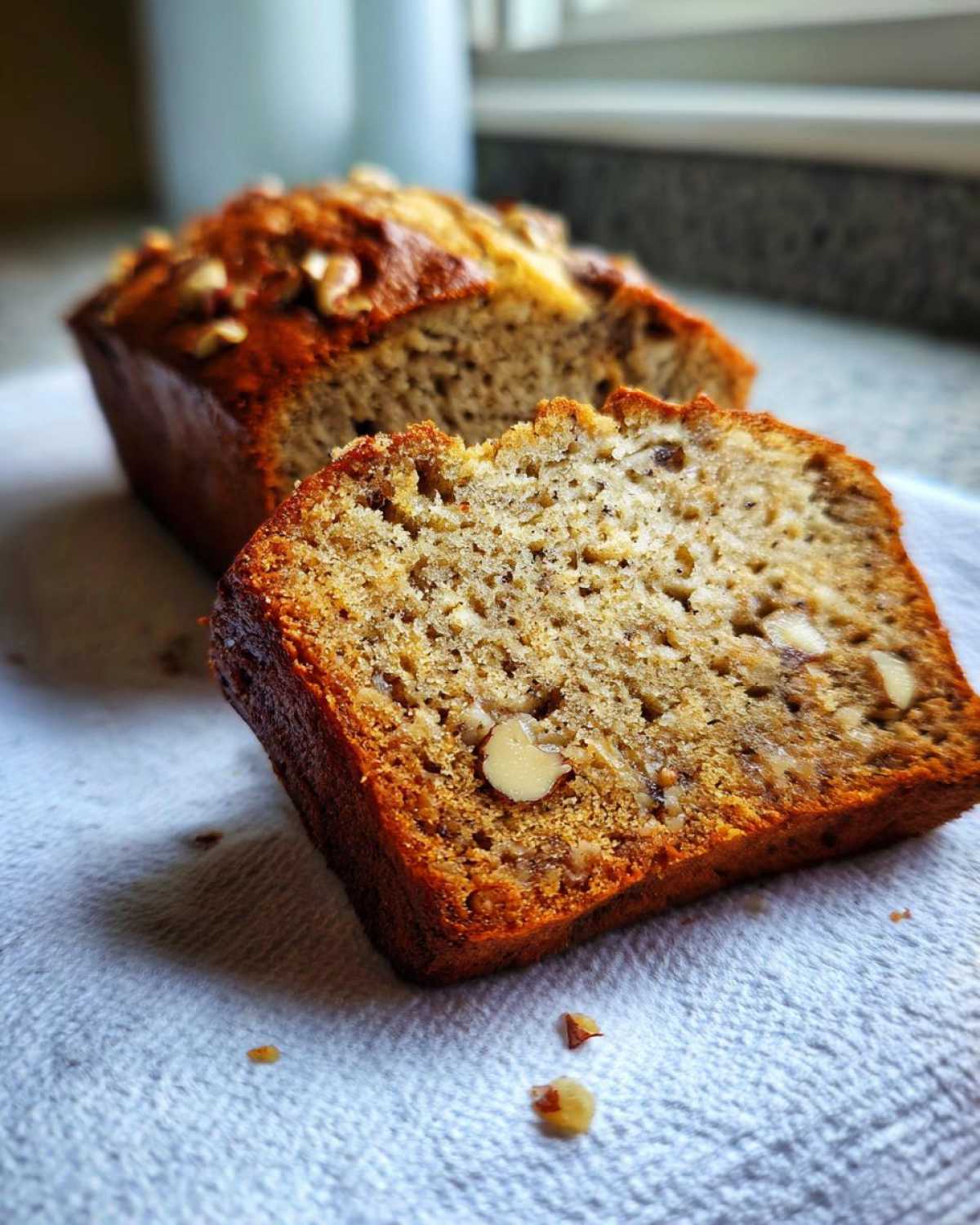 Close-up of a slice of moist sugar free banana bread showing walnuts inside, with the rest of the loaf in the background.