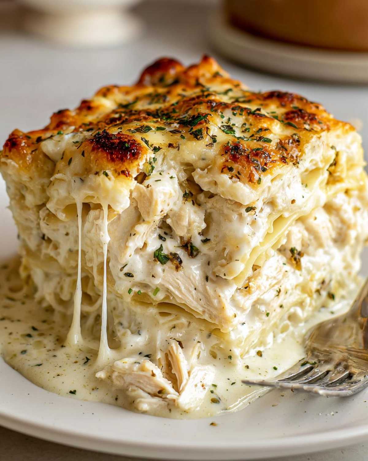 A decadent, cheesy slice of 8-layer chicken lasagna with creamy white sauce oozing out.
