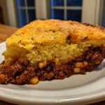 A thick slice of Tamale Pie showing a savory ground meat filling topped with golden cornbread.