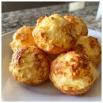 Close-up of several golden-brown, puffy brazilian cheese bread balls stacked on a white plate.