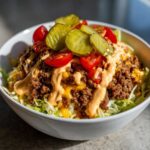 A close-up view of a hearty cheeseburger bowl featuring seasoned ground beef, melted cheese, lettuce, tomatoes, pickles, and special sauce.