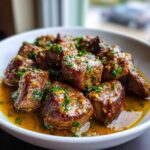 Close-up of tender crockpot steak bites coated in a rich, buttery garlic sauce and topped with fresh parsley.