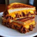 Close-up of a stacked, grilled sandwich featuring savory meat filling and melted cheddar cheese inside toasted texas toast sloppy joes.
