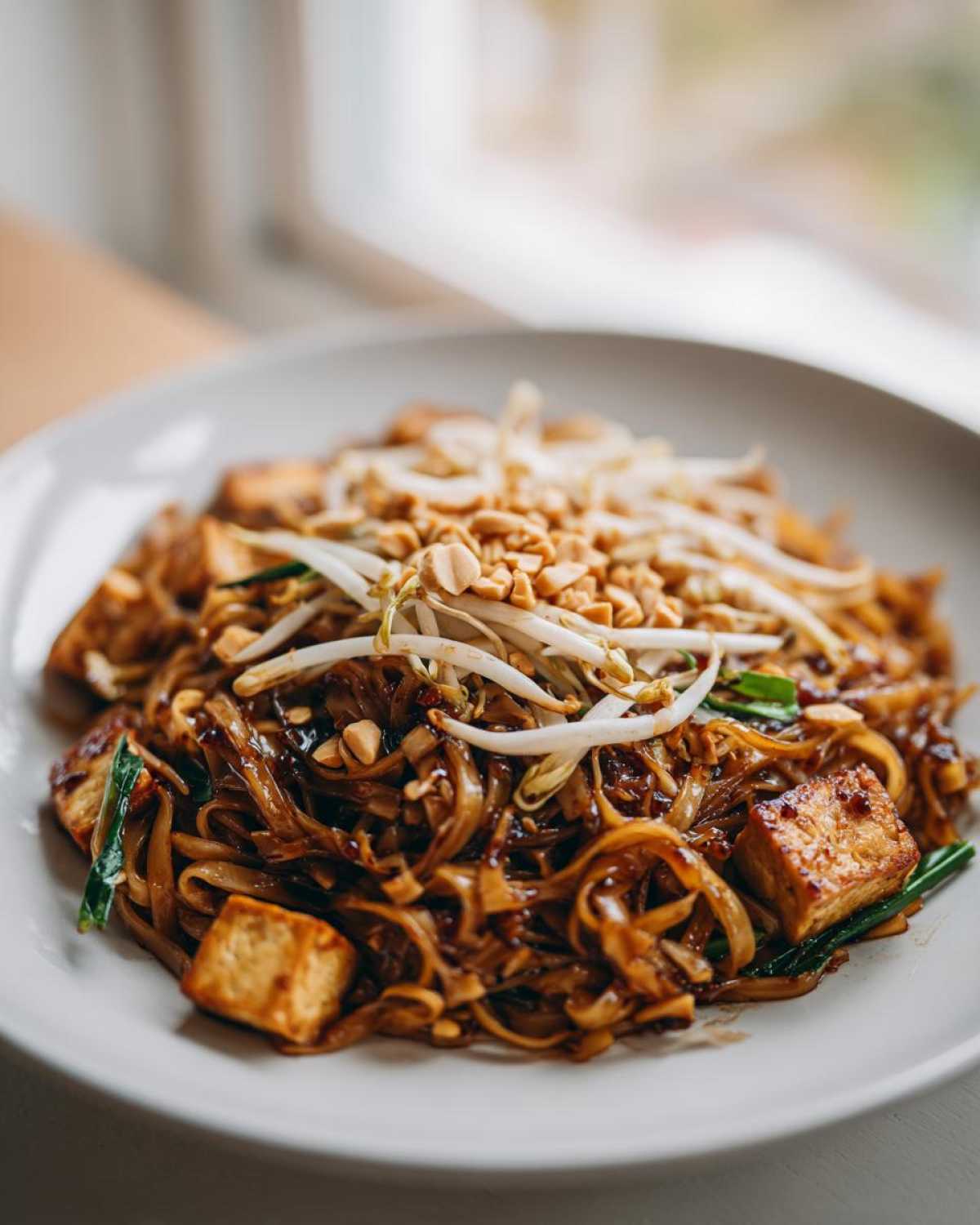 A close-up of a plate of saucy Pad Thai noodles topped with fresh bean sprouts and crushed peanuts.