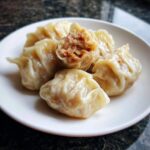 Close-up of steamed Traditional Chinese Dumplings on a white plate, one dumpling is broken open showing the savory meat filling.