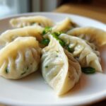 Close-up of several steamed Traditional Chinese Dumplings arranged on a white plate, garnished with sliced green onions.