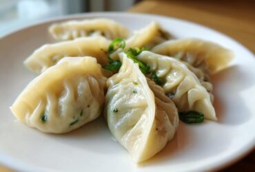 Close-up of several steamed Traditional Chinese Dumplings arranged on a white plate, garnished with sliced green onions.