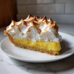 A perfect slice of lemon meringue pie showing thick lemon curd and torched meringue peaks.