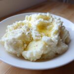 A close-up of fluffy, creamy mashed potatoes topped with melted butter and cracked black pepper.
