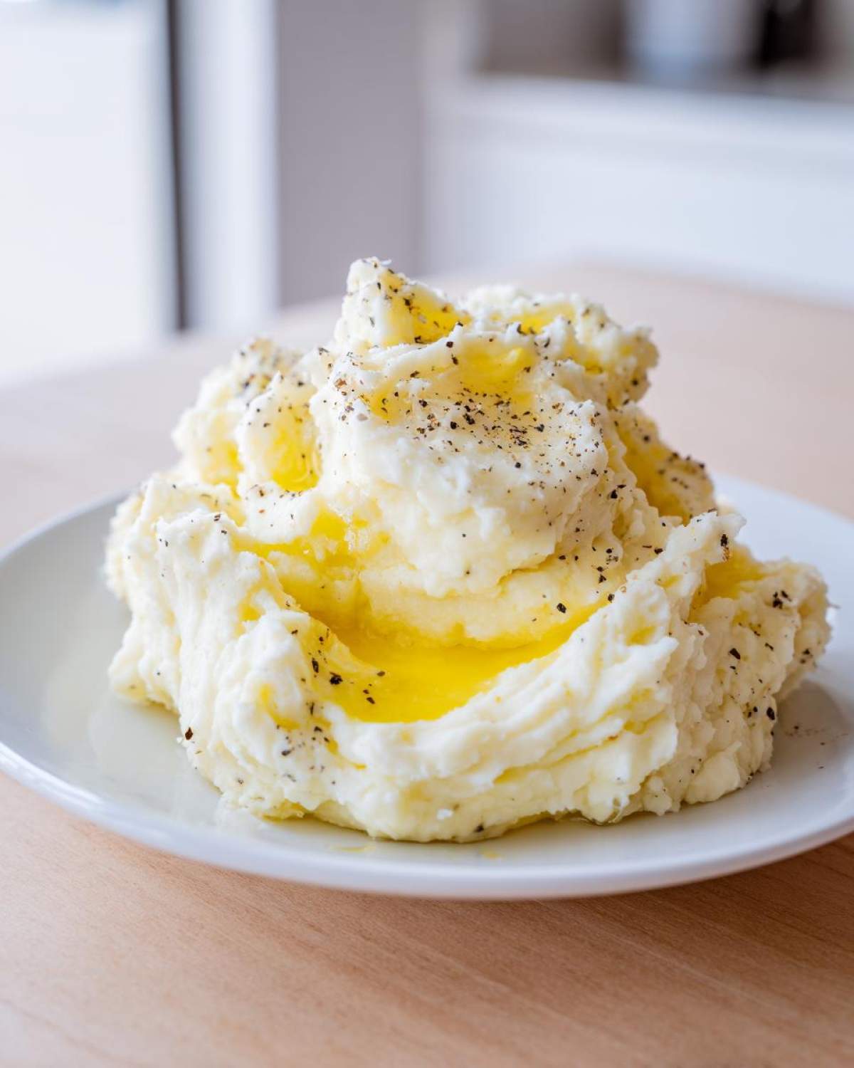 A generous serving of creamy mashed potatoes topped with melted butter and cracked black pepper.