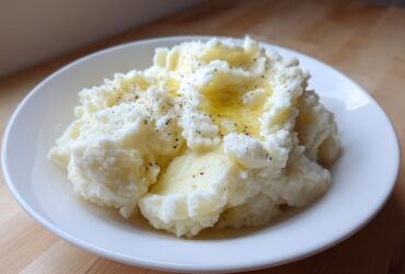A close-up of fluffy, creamy mashed potatoes topped with melted butter and cracked black pepper.