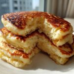 Close-up of a stack of incredibly fluffy pancakes, showing the airy interior texture, with a bite taken out.