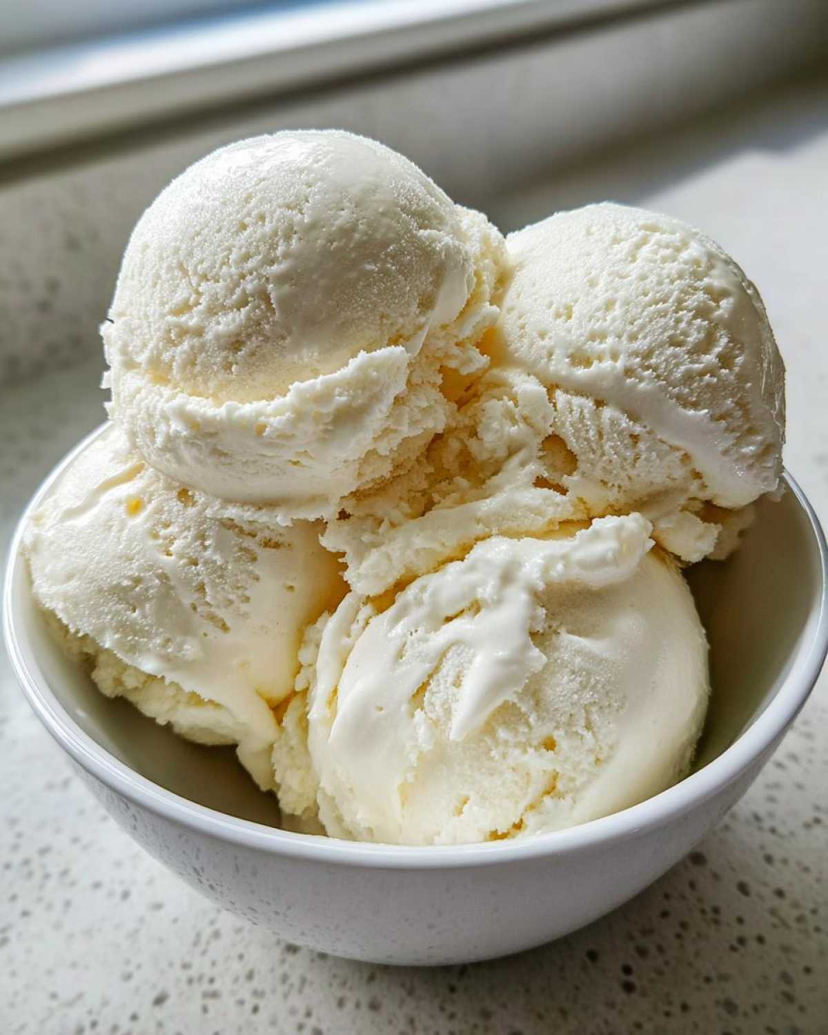 Close-up of four scoops of creamy vanilla protein ice cream served in a small white bowl.