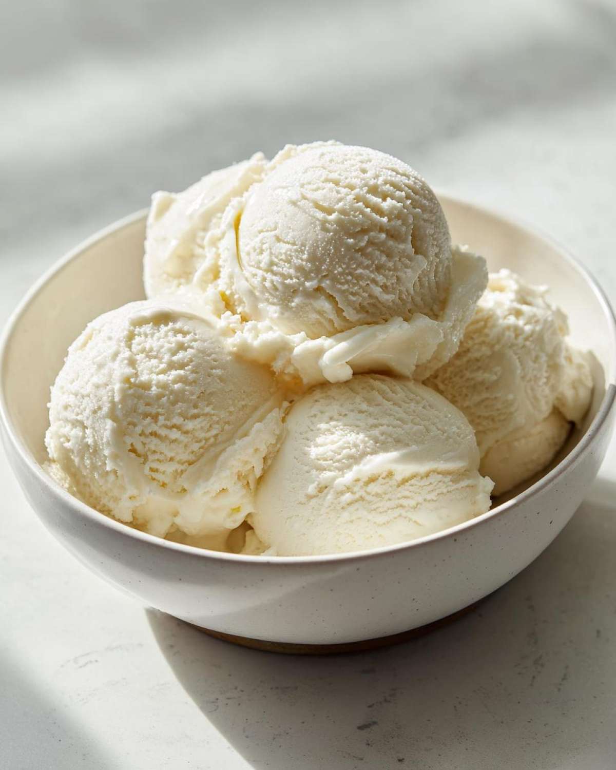 Several scoops of creamy, white protein ice cream served in a speckled ceramic bowl.