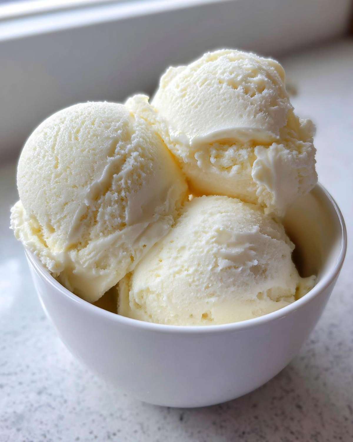 Three scoops of creamy, vanilla-colored protein ice cream served in a small white bowl.