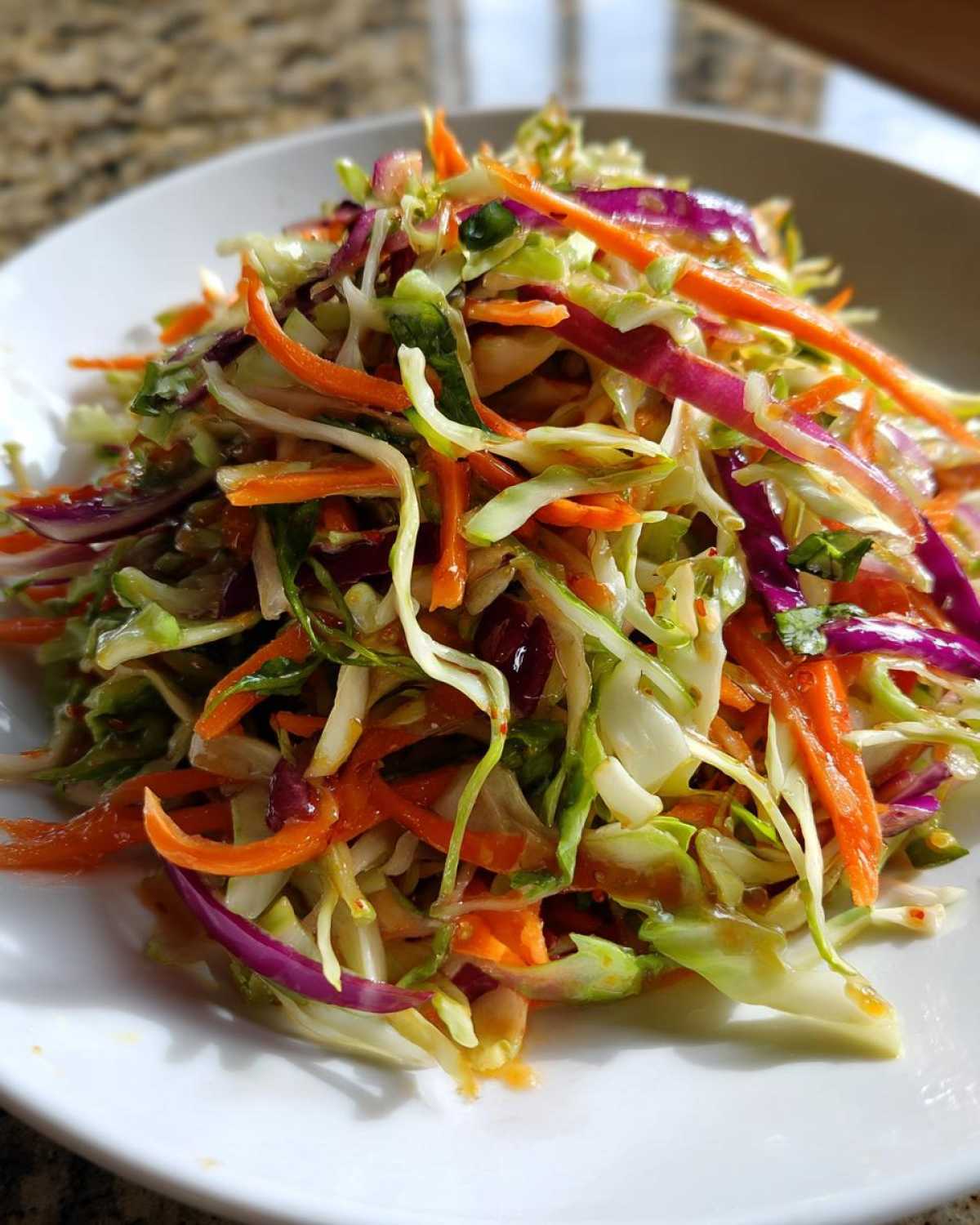 Close-up of a vibrant cabbage salad featuring shredded green and purple cabbage mixed with julienned carrots, coated in a light dressing.