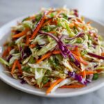 Close-up of a vibrant, freshly tossed cabbage salad featuring shredded green and red cabbage, carrots, and green onions.