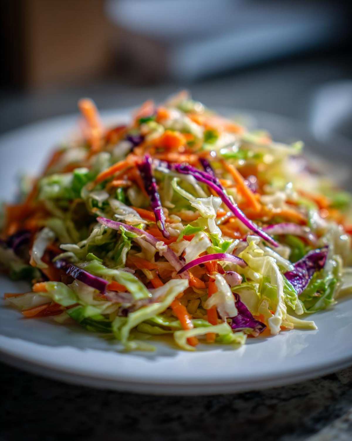Close-up of a vibrant cabbage salad featuring shredded green cabbage, red cabbage, and carrots on a white plate.