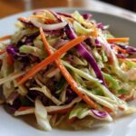 Close-up of a vibrant, freshly dressed cabbage salad featuring shredded green and red cabbage, julienned carrots, and red onion slices.