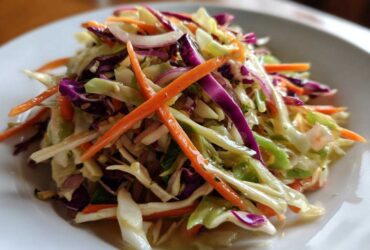Close-up of a vibrant, freshly dressed cabbage salad featuring shredded green and red cabbage, julienned carrots, and red onion slices.