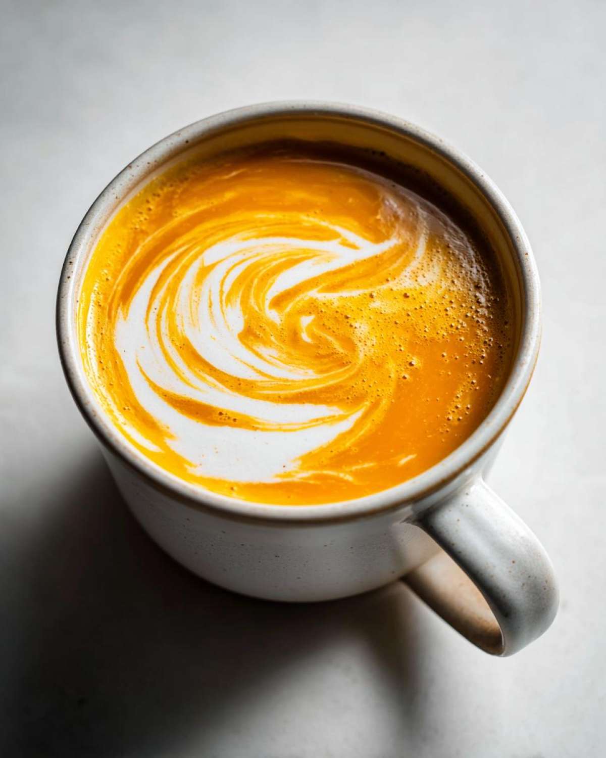 Overhead view of vibrant orange squash soup topped with a white cream swirl in a speckled mug.