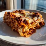 A delicious, layered slice of hearty Lasagna with rich meat sauce and melted cheese, served on a white plate.