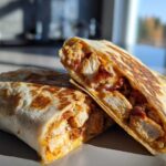 Two halves of an Air Fryer Crispy Chicken Bacon Ranch Wrap, showing chunks of chicken, bacon, and ranch filling inside a toasted tortilla.