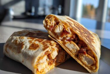 Two halves of an Air Fryer Crispy Chicken Bacon Ranch Wrap, showing chunks of chicken, bacon, and ranch filling inside a toasted tortilla.
