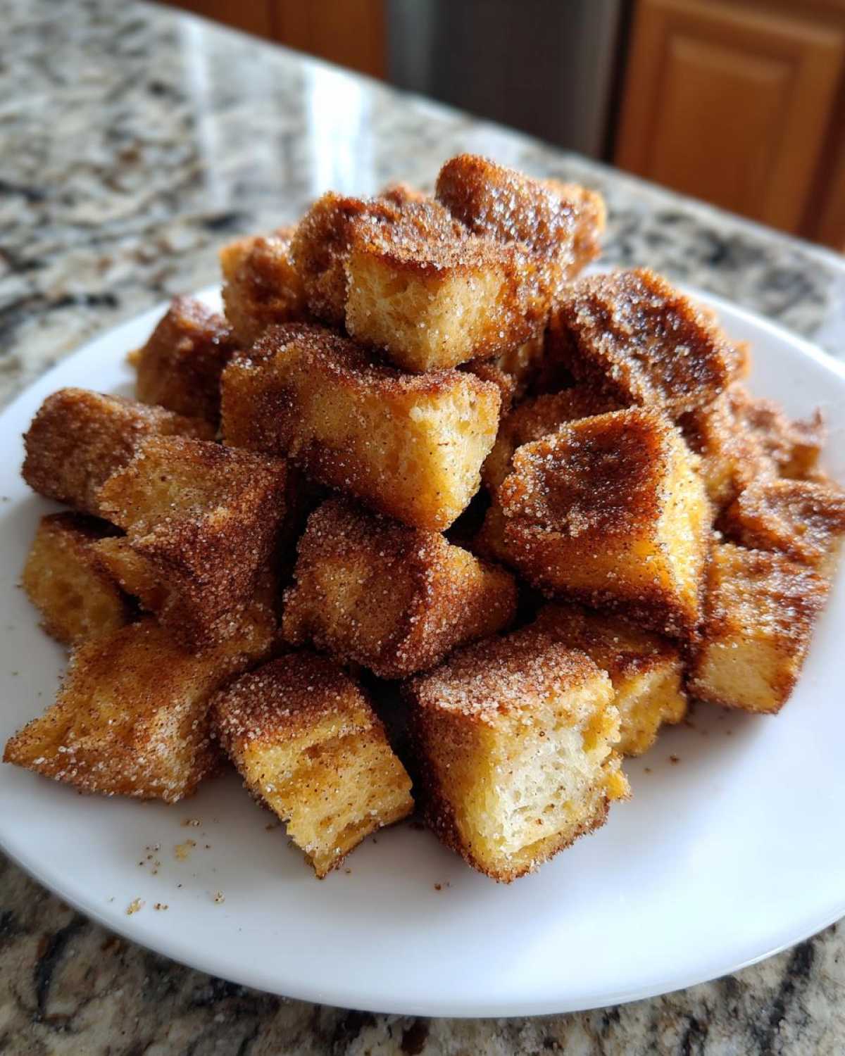 Close-up of a white plate piled high with Air Fryer Crispy Cinnamon French Toast Bites coated in sugar.