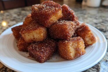 A close-up of a white plate piled high with Air Fryer Crispy Cinnamon French Toast Bites coated in cinnamon sugar.