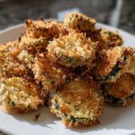 A pile of golden brown, crispy Air Fryer Crispy Garlic Dill Pickles slices served on a white plate.
