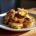 A pile of golden brown, crispy Air Fryer Crispy Garlic Dill Pickles slices stacked on a white plate.