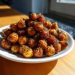 A mound of golden brown Air Fryer Crispy Garlic Herb Chickpeas seasoned with herbs, served on a white plate.