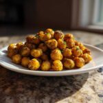 A mound of golden brown Air Fryer Crispy Garlic Herb Chickpeas seasoned with herbs, served on a white plate.