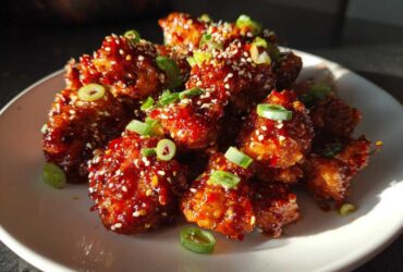 Close-up of glistening Air Fryer Crispy Korean Chicken Bites coated in spicy sauce, topped with sesame seeds and sliced green onions.